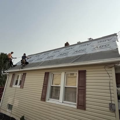 Two roofers installing synthetic underlayment on a house mid-roof-replacement in Spring Grove, Pennsylvania